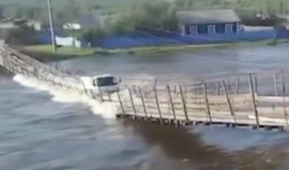 増水した川の木造橋を渡る車