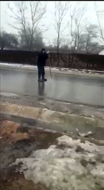 長靴と棒で凍った道路を滑る男性